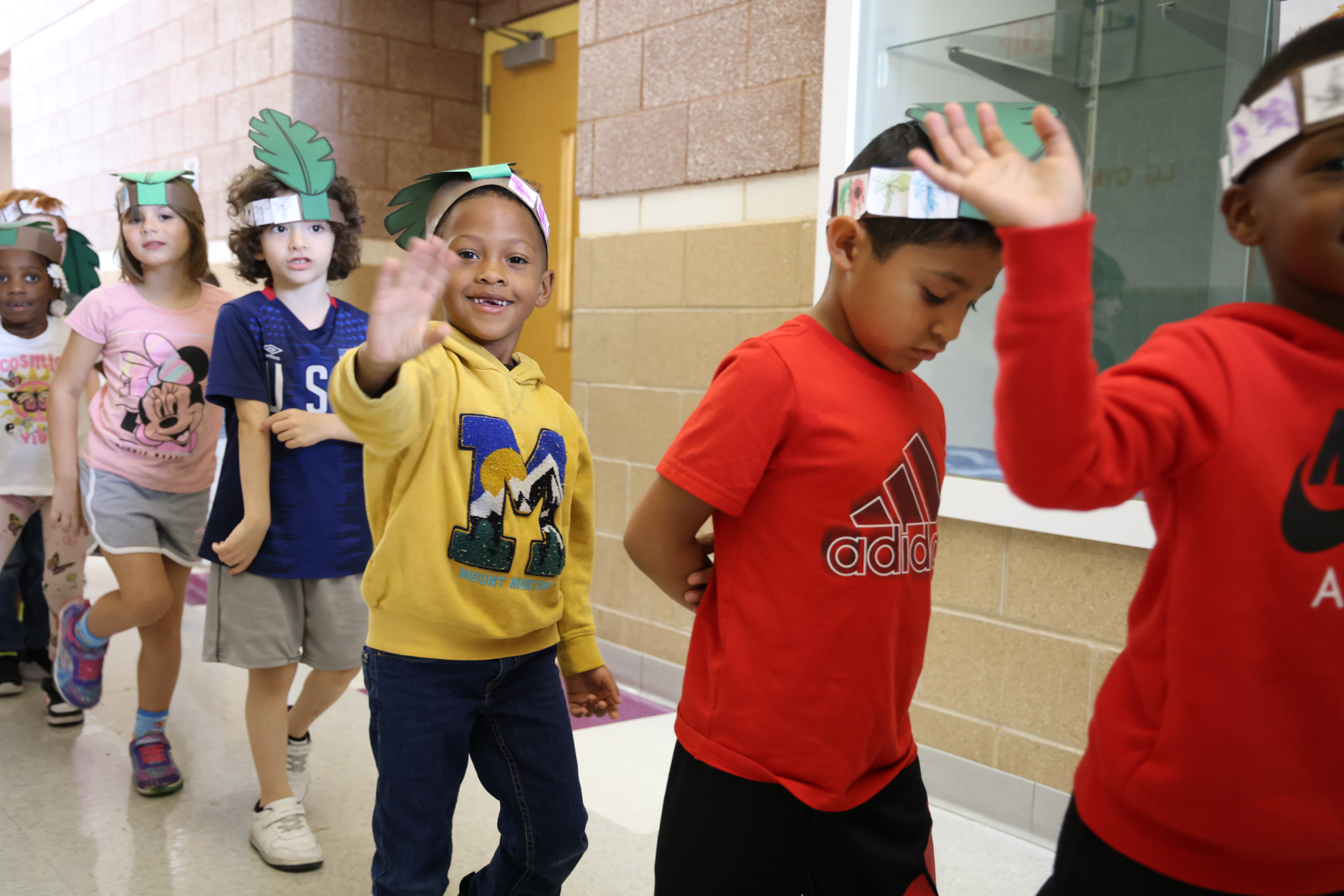 Kindergarten students walk down the halls of a school while one of them waves